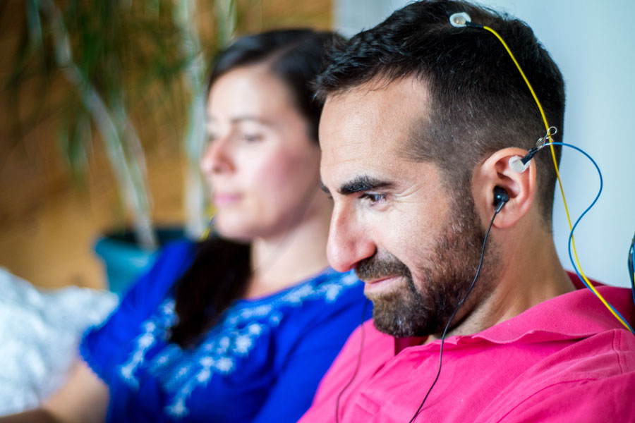 Neurofeedback for Adults | Stress Relief & Cognitive Training Man using NeurOptimal® neurofeedback for brain training and stress relief while sitting next to a woman.
