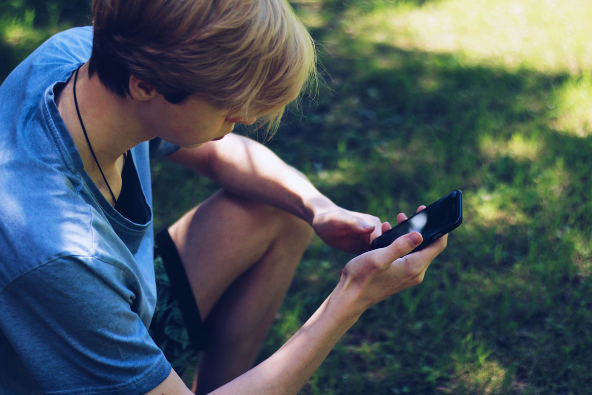 Teen & Child Therapy | Online & In-Person Counseling | Mount North Teen sitting outside using a mobile phone, representing accessible online therapy and counseling for teens at Mount North.