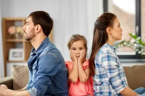 A young girl sits between two parents facing away from each other, symbolizing the emotional impact of parental conflict during a custody battle.